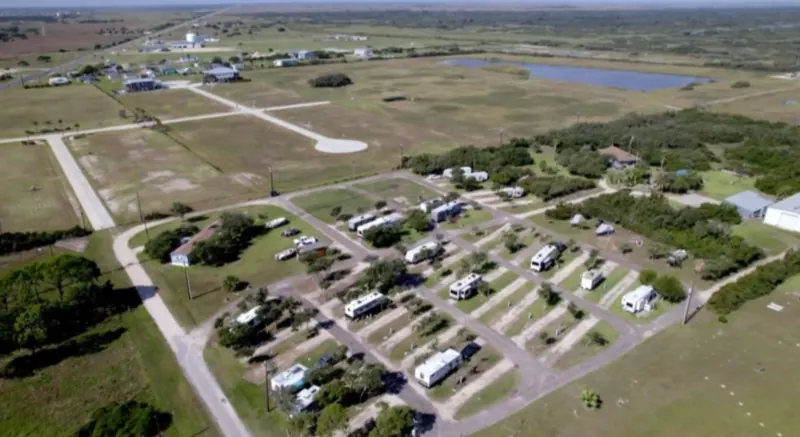 Aerial view of Bay Breeze RV Park from above the trees, with the pond and open coastal land beyond the sites