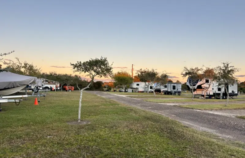 Boats on trailers parked on the grass beside RV sites at Bay Breeze RV Park, under an evening sky
